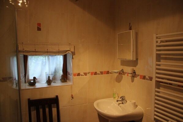 A bathroom with a sink, mirror, towel rack, and a window with decorative items. - Detached Cottage With Heated Pool (Paule)