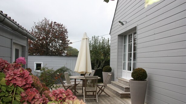 A wooden deck with outdoor furniture, a potted plant, and a white umbrella.