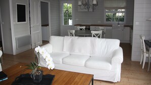A white interior with a white sofa, wooden coffee table, and a dining area with a table and chairs.