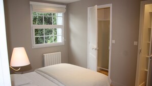 A bedroom with a bed, a window with a view of greenery, a radiator, and an open door to a closet.