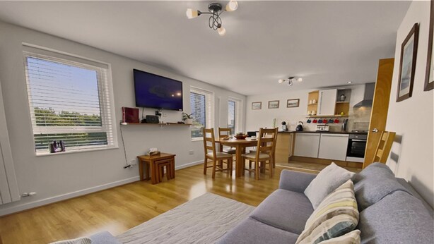 A modern living room with a sofa, a dining area with chairs, a kitchen with cabinets, and a TV mounted on the wall.