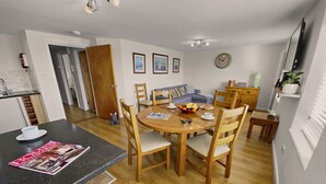 A modern kitchen with a dining area, wooden furniture, and a clock on the wall.