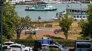 Uitzicht op het water met een opvallende, zeilvormige brug, een groene veerboot en een park met bankjes.