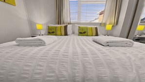 A neatly made bed with white linens and pillows, two bedside lamps, and a window with curtains.