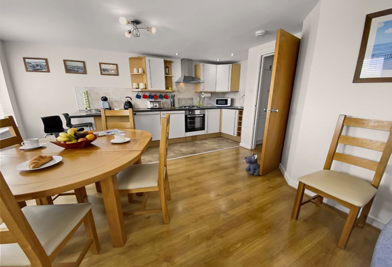 Une cuisine moderne avec des meubles blancs, une table à manger en bois avec des chaises et un petit îlot de cuisine.