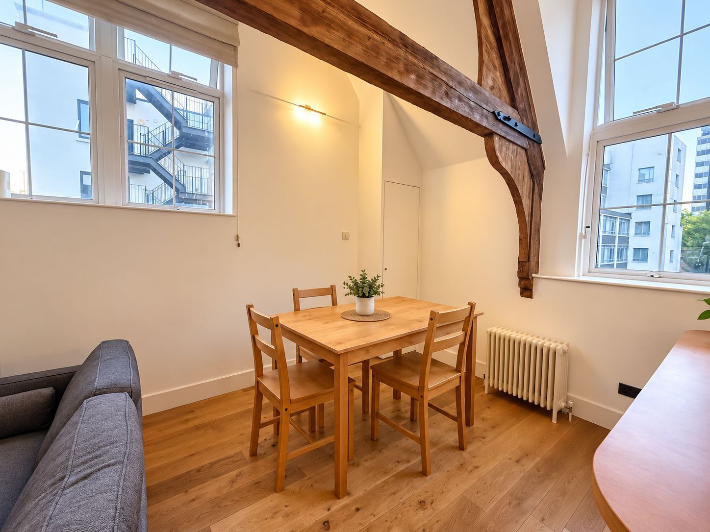 A dining area with a wooden table and chairs, a potted plant, and a view of a building with a staircase.