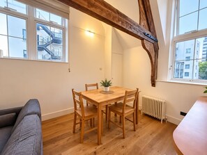 Un comedor con una mesa y sillas de madera, una planta en maceta y vista a un edificio con escaleras.