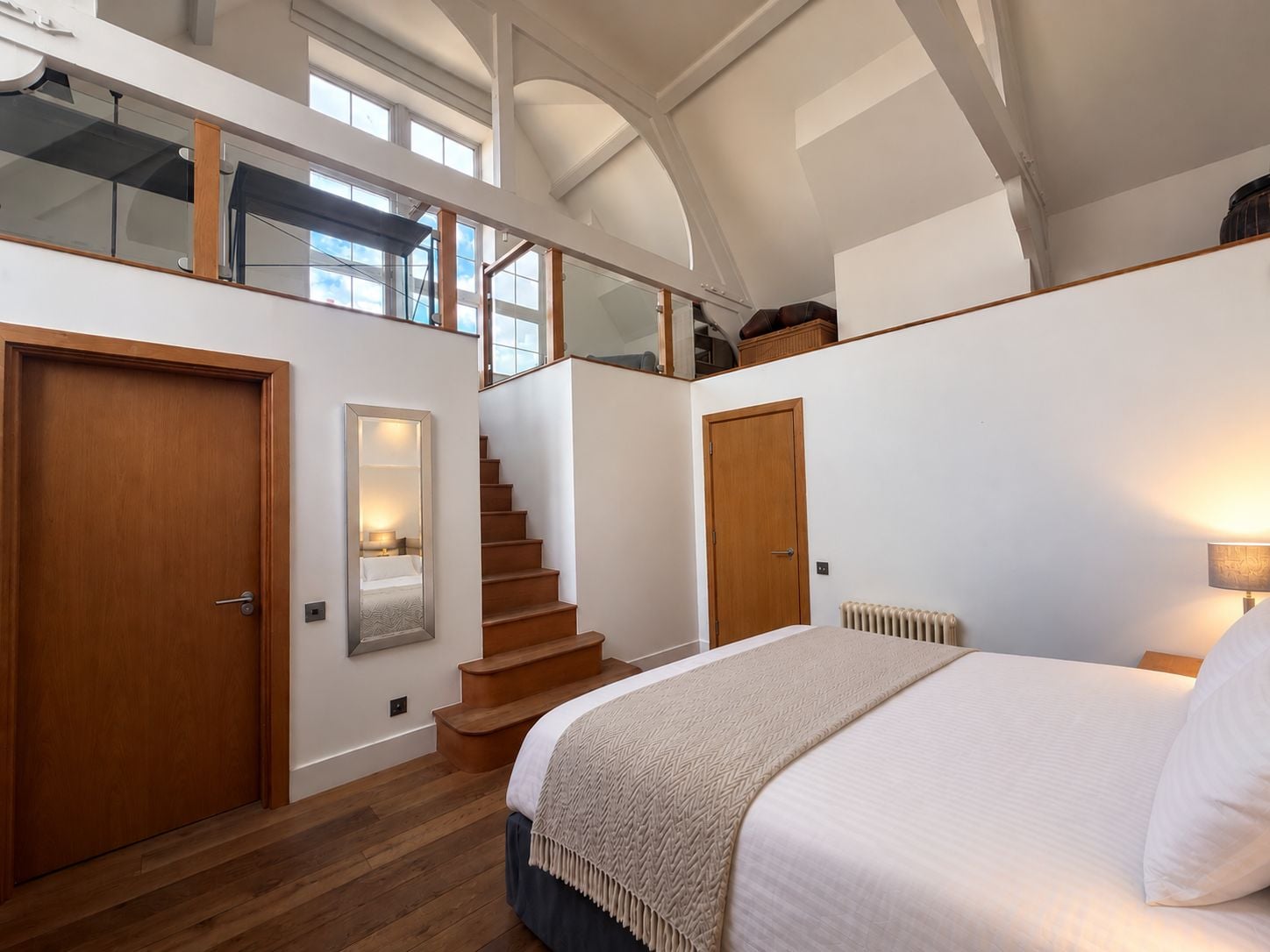 A bedroom with a large bed, a wooden staircase, and a view of the sky through the ceiling.