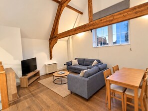 A modern living room with a sectional sofa, a TV, a wooden dining table, and a large window with a view. - A unique apartment in the heart of central London. (London)