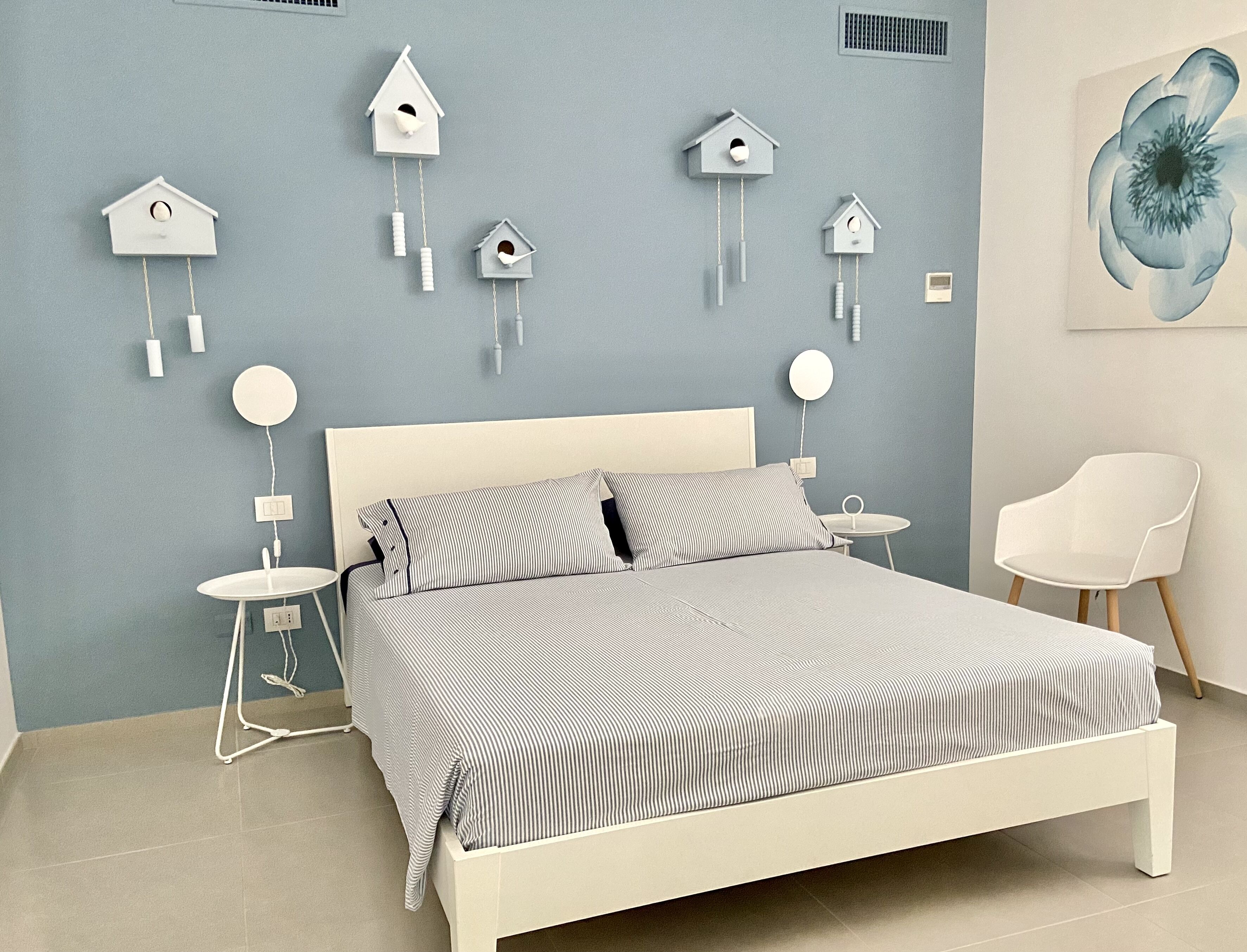 Ein Schlafzimmer mit einem Bett, zwei Nachttischen, einem Sessel und mehreren an der Wand befestigten Vogelhausdekorationen.
