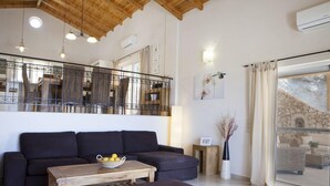 Una sala de estar moderna con techo de madera, un sofá negro, una mesa de centro de madera y vista a una chimenea de piedra a través de una puerta de cristal.