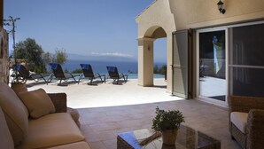 Un espacio cubierto con mobiliario al aire libre, vistas al mar, una puerta corrediza de vidrio y una planta en maceta.