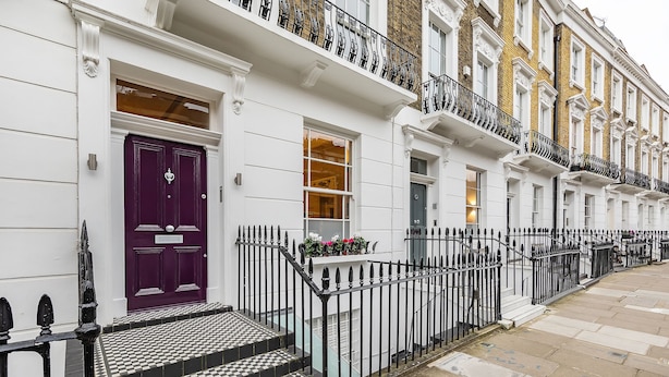 A row of white townhouses with black and white checkered steps, a purple door, and black iron railings.