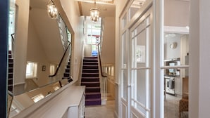 A hallway with a staircase, a mirror, and a kitchen area with cabinets and appliances.
