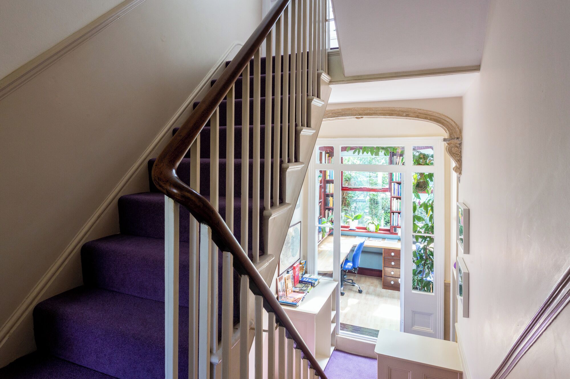 A staircase with a wooden handrail leading to a room with a desk, chair, and bookshelves.