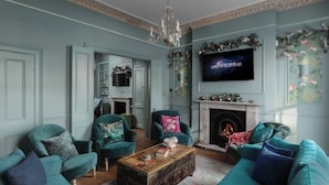 A living room with teal furniture, a fireplace, and a flat-screen TV displaying "UNIVERSAL".