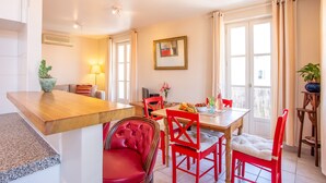 A dining area with a wooden table, red chairs, and a red upholstered chair. There is a potted plant on the table and a lamp on the wall. - Antibes Old Town, Sunny, South facing apartment 2 Balconies, fully air condition (Antibes)