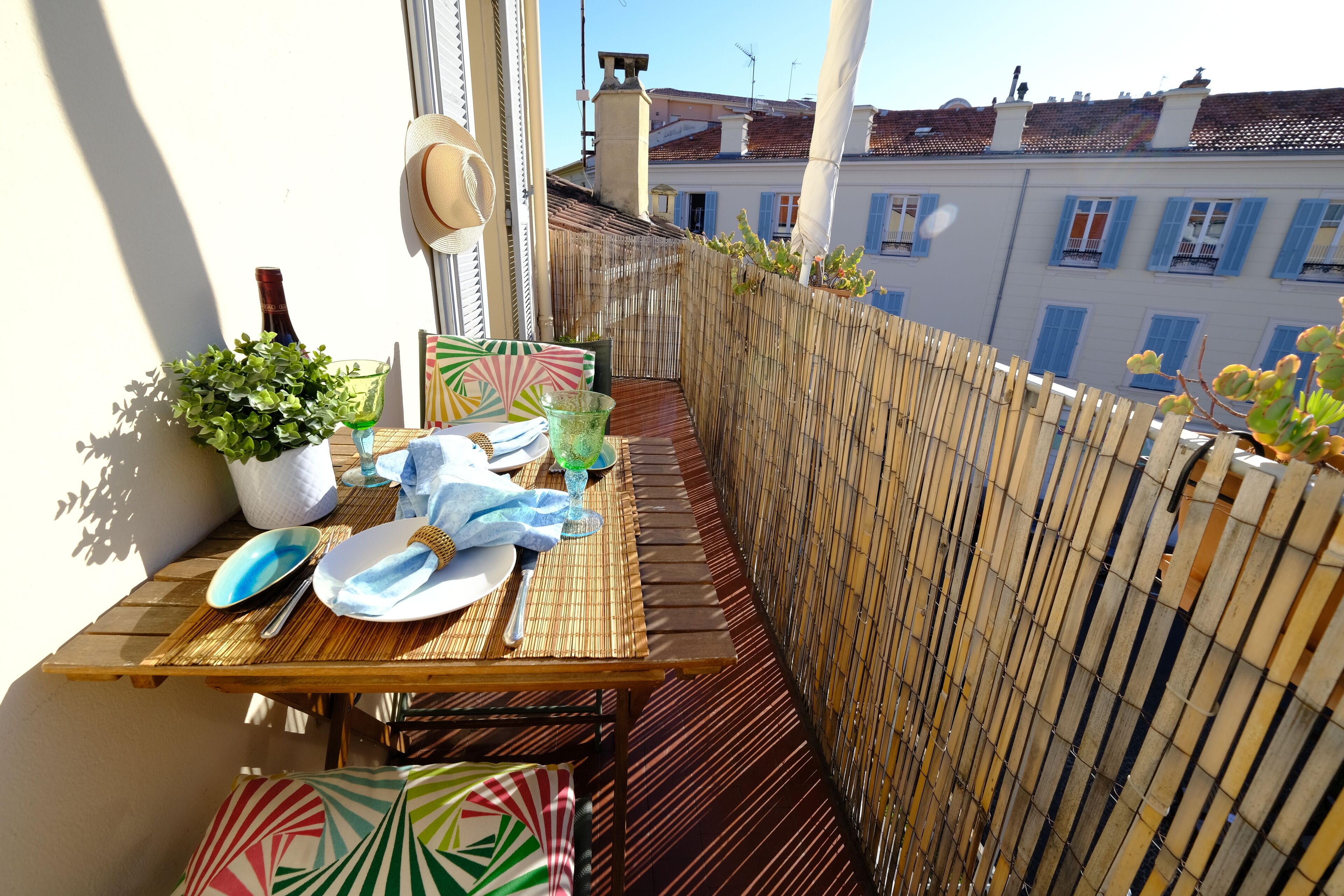 A balcony with a table set for dining, a potted plant, and a wicker basket.