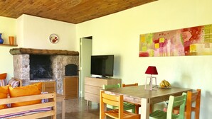 Ein gemütliches Wohnzimmer mit Kamin aus Stein, Holzmöbeln, einem Fernseher und einem farbenfrohen Gemälde an der Wand.
