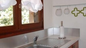 Eine Küche mit einer Holzausziehtafel, einer Edelstahlspüle und einem Fenster mit weißen Vorhängen.