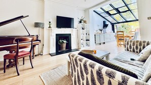 Un amplio salón con un piano de cola, chimenea, televisor y un gran ventanal con vistas al exterior.