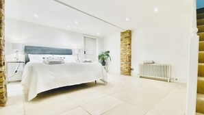 A spacious bedroom with a large bed, a stone accent wall, a radiator, and a staircase. - Large Richmond Garden Apartment 4 Bd/3 Bth w Parking (child/pet friendly!) (Richmond)