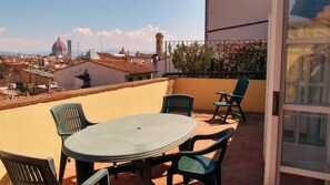 Un balcón con mesa y sillas, con vistas a un paisaje urbano que incluye edificios históricos y una estructura en forma de cúpula.