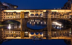 Un puente de piedra con tres arcos sobre un cuerpo de agua tranquilo, que refleja los edificios a ambos lados.