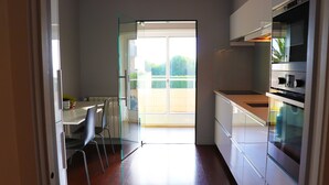 Een moderne keuken met een eethoek, een glazen deur naar een balkon en een inbouwoven.