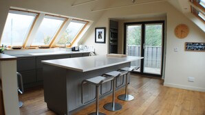 Une cuisine moderne dotée d’un grand îlot central, de tabourets de bar, de fenêtres de toit et offrant une vue à travers la porte vitrée.