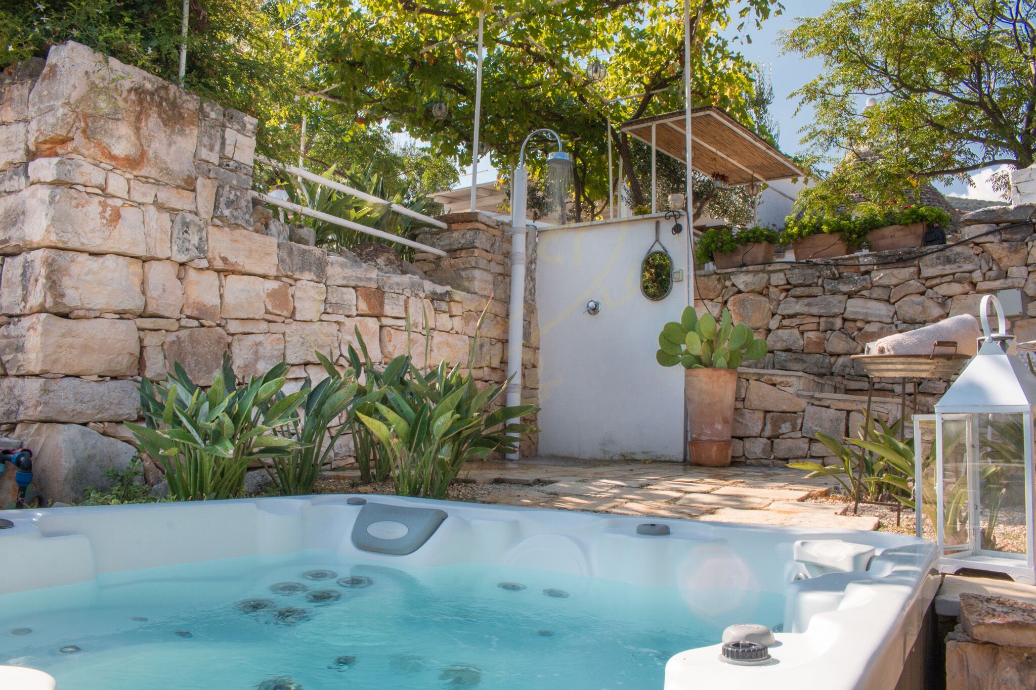 Zona de hidromasaje con paredes de piedra, plantas en macetas y una pérgola.