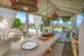 Ein Holztisch mit einem weißen Teller und einer Schüssel, vor einer malerischen Kulisse mit Blick auf das Meer und Grünflächen.