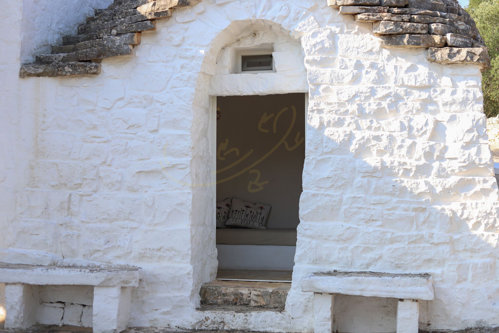 A white stone building with a small arched doorway and a bench inside.