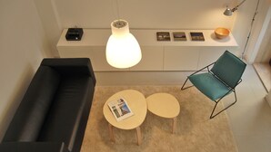 Een moderne woonkamer met een zwarte bank, twee ronde tafels, een groene fauteuil en een witte plank met decoratieve objecten.