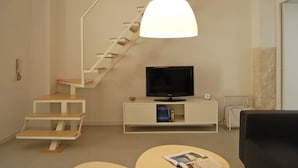 Een moderne woonkamer met een trap, een flatscreen televisie, een witte salontafel en een tijdschrift op een ronde tafel.
