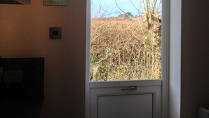 Habitació amb finestra que dona a un camp, una porta i un rètol fixat a la paret.