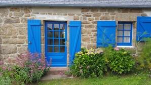Ein Steinhaus mit blauer Tür und Fensterläden, umgeben von einem Garten mit verschiedenen Blumen.