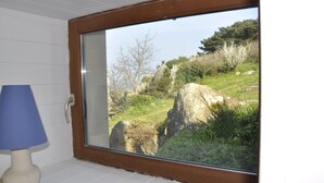 Ein Zimmer mit einem großen Fenster mit Blick auf einen grasbewachsenen Hügel mit Felsen und Bäumen.