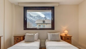 Een kamer met twee bedden, een raam met uitzicht op de bergen, een lampje op een nachtkastje en een houten kast.