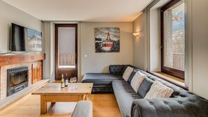 Een woonkamer met een open haard, een bank, een houten tafel met wijnglazen en een schilderij van de Eiffeltoren.