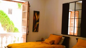 Ein Zimmer mit zwei Betten, einer Hängelampe, einem Fenster mit Blick auf Grünflächen und einer Tür, die nach draußen führt.