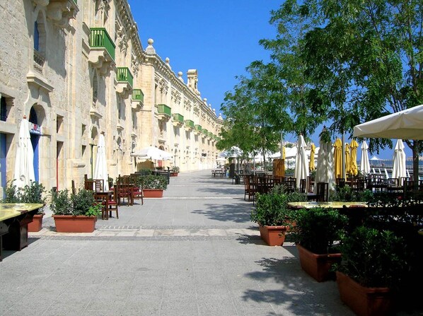 Un patio con mobiliario exterior, plantas en macetas y un edificio de arquitectura ornamentada.