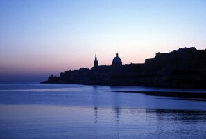A coastal cityscape at dusk with a prominent church and a tall tower silhouetted against the sky. - Grand Harbour, Valletta, Malta - sleeps six (Ta'Liesse)