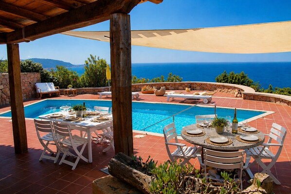 A poolside area with a table set for dining, lounge chairs, and a view of the sea.