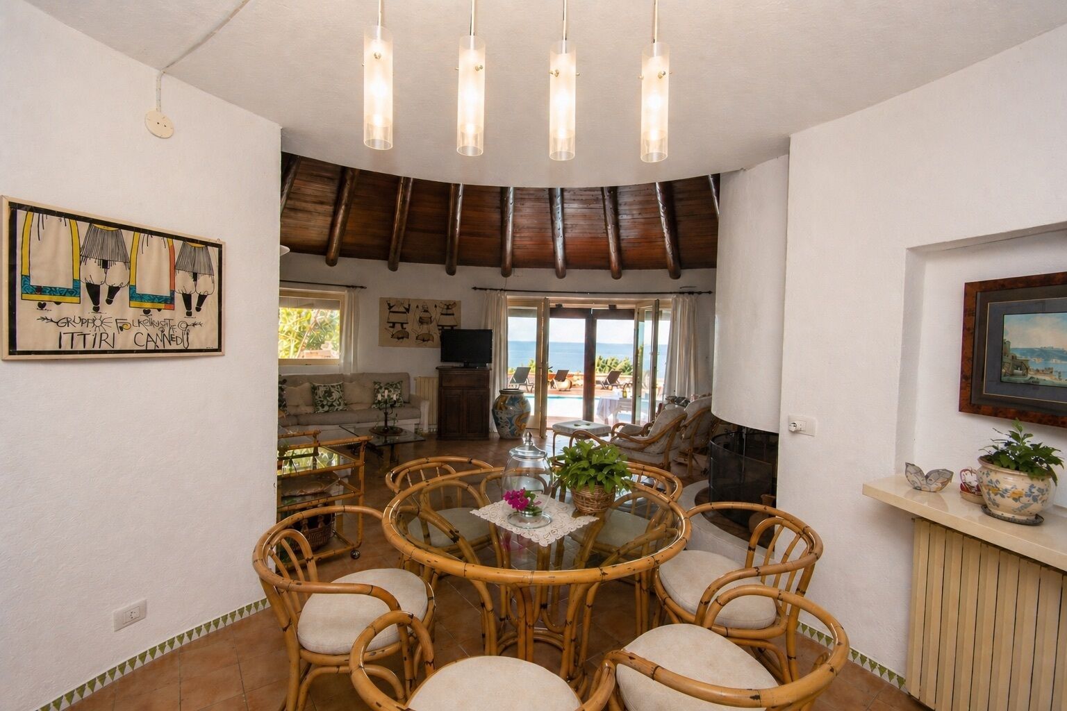 A dining area with wicker chairs, a round table, and pendant lights.
