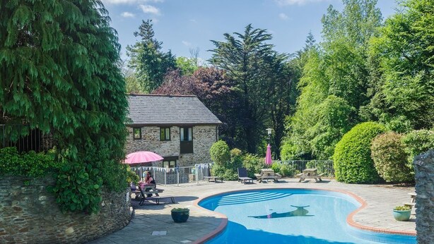 A swimming pool with a stone building in the background, surrounded by lush greenery.
