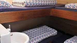 Een stapelbed met beddengoed met patroon, een witte wastafel en houten wanden.