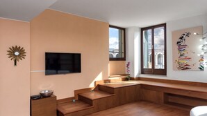 A modern bedroom with a wooden staircase, a flat-screen TV mounted on the wall, and a large window offering a city view. - Appartamento storico con balconi vista Arena (Verona)