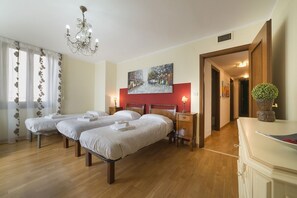 Hotellihuone, jossa on kolme sänkyä, kattokruunu, taulu seinällä ja puinen kaappi.