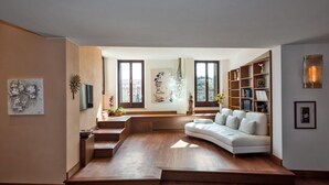 A modern living room with a curved sofa, wooden flooring, and a bookshelf. - Appartamento storico con balconi vista Arena (Verona)